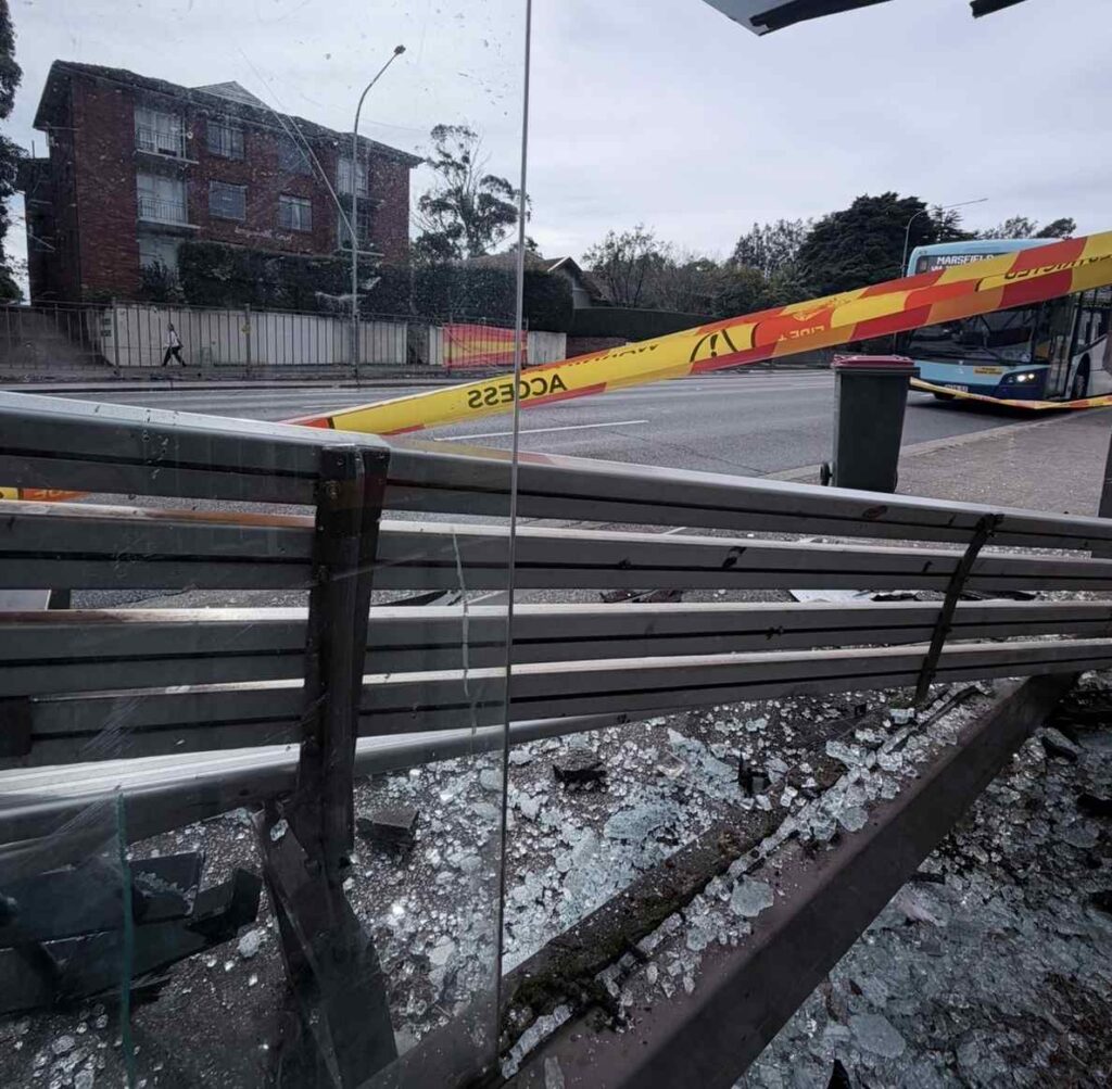 Damaged Lane Cove bus shelter taped off with buckled bench and shattered glass on Longueville Road