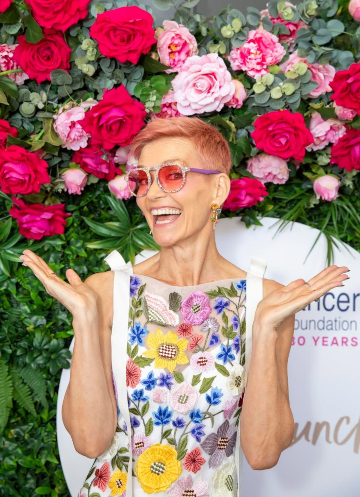 Jessica Rowe laughing in front of the flower wall at the 2025 Sydney Breast Cancer Foundation Ladies Lunch