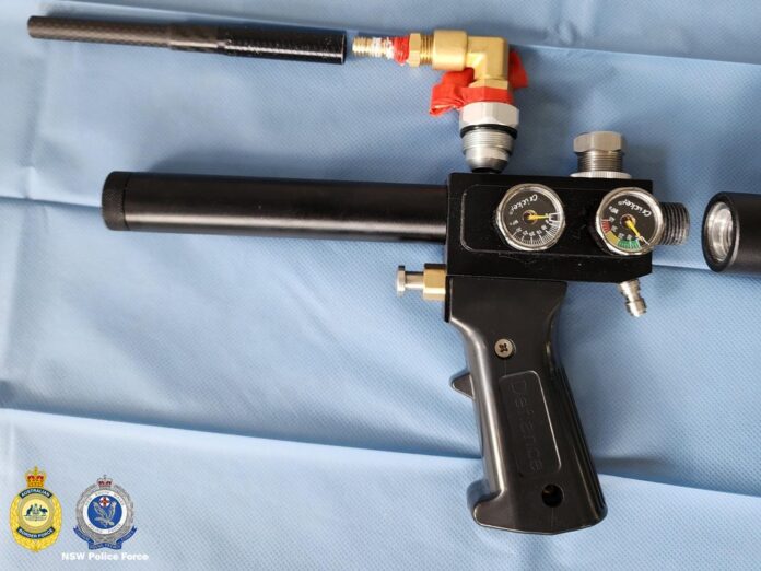 lane-cove-west-firearms-raid-airgun-featured Black airgun with a carbon barrel and air cylinder standing upright in a cluttered room next to a printer