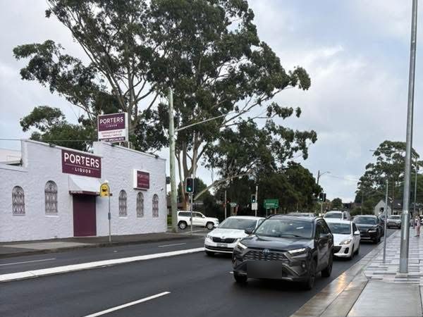 White bottle shop with purple Porters Liquor signs beside a busy road and traffic lights, gum trees behind