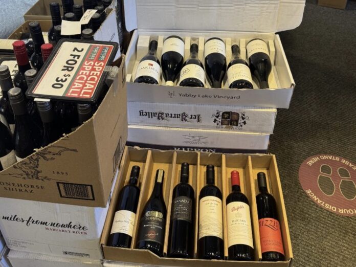 Two open cases of red wine on top of stacked boxes in a bottle shop, with a 2 for $30 special sign