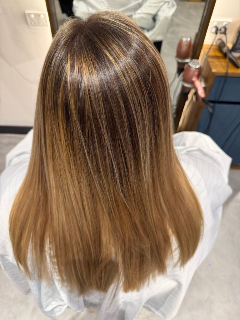 Long, straight brunette hair with soft caramel balayage at K Avenue Hair & Beauty.