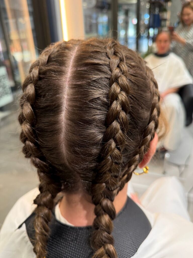 Two neat braids running from a centre part on a young client at K Avenue Hair & Beauty.